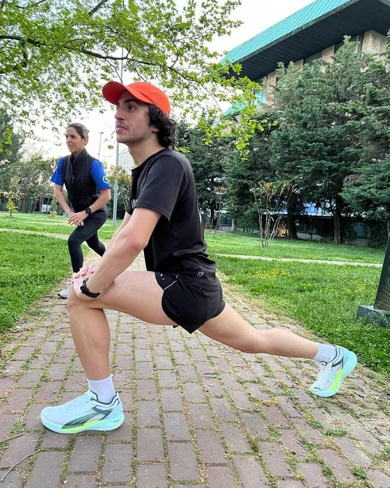 Un homme en tenue de sport PUMA au premier plan est en train de s’étirer dans un parc