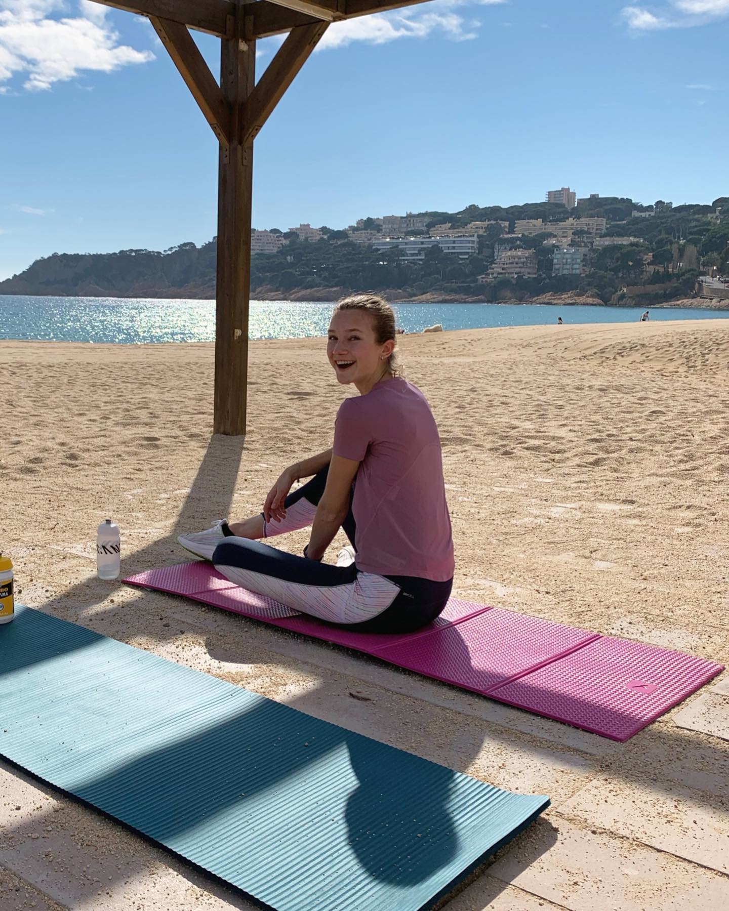 A woman in PUMA yoga clothes is sitting on a yoga mat on the beach