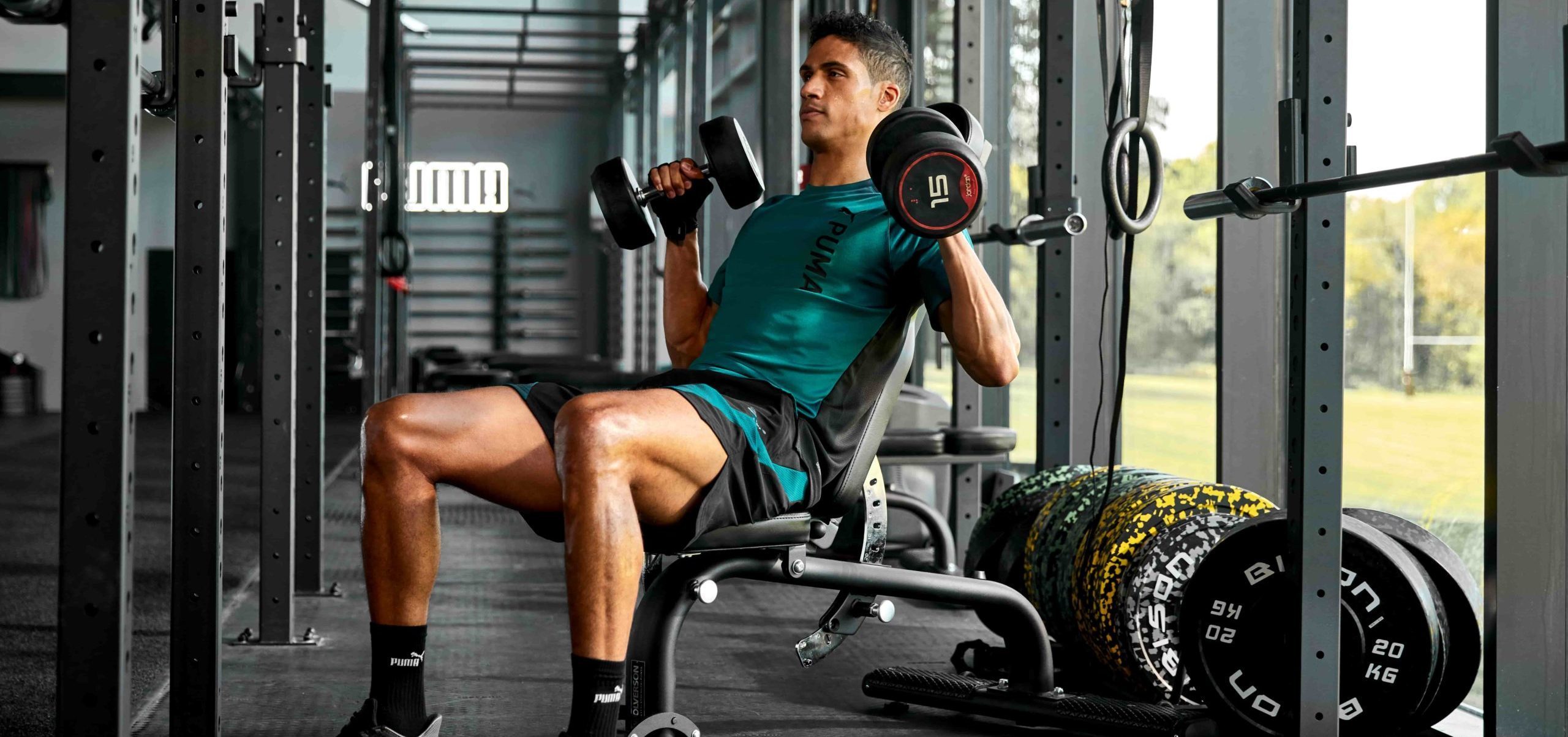 Un homme en tenue de sport PUMA est dans une salle de fitness en train de faire des exercices de musculation des bras