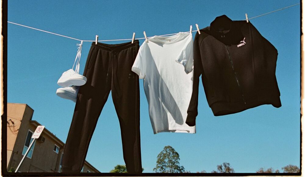 witte puma-sneakers, zwarte puma-joggingbroek, wit puma-shirt en zwart puma-sweatjack aan een waslijn