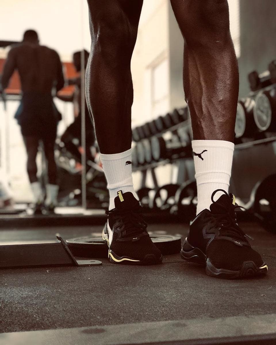  Iemand draag een paar zwarte PUMA sneakers met hoog opgetrokken witte PUMA sokken in een fitnessruimte. 