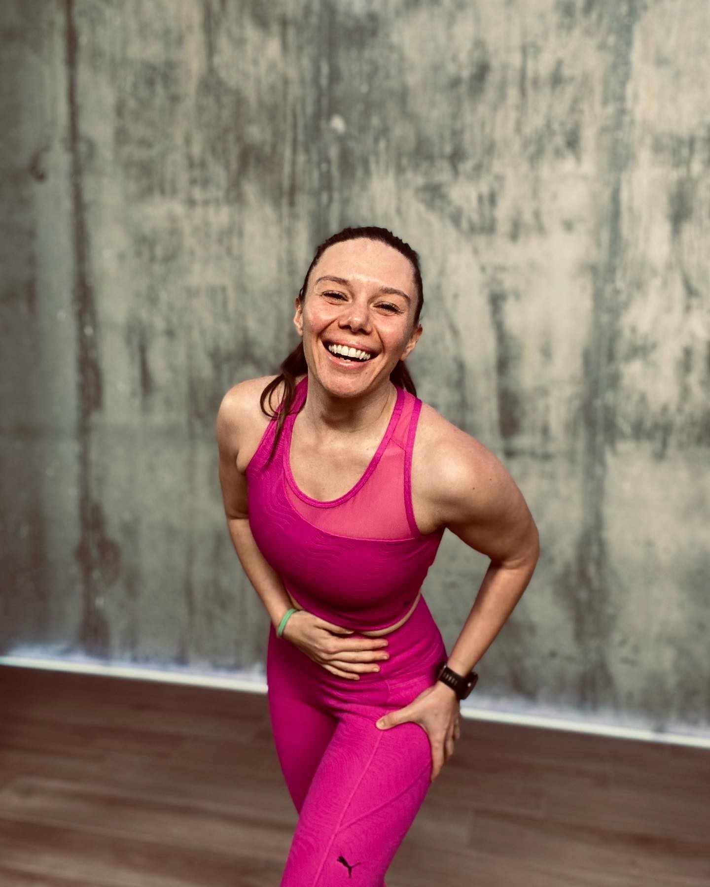 Frau in pinken PUMA Leggings und Sport-BH lächelt nach dem Hula Hoop Training verschwitzt in die Kamera