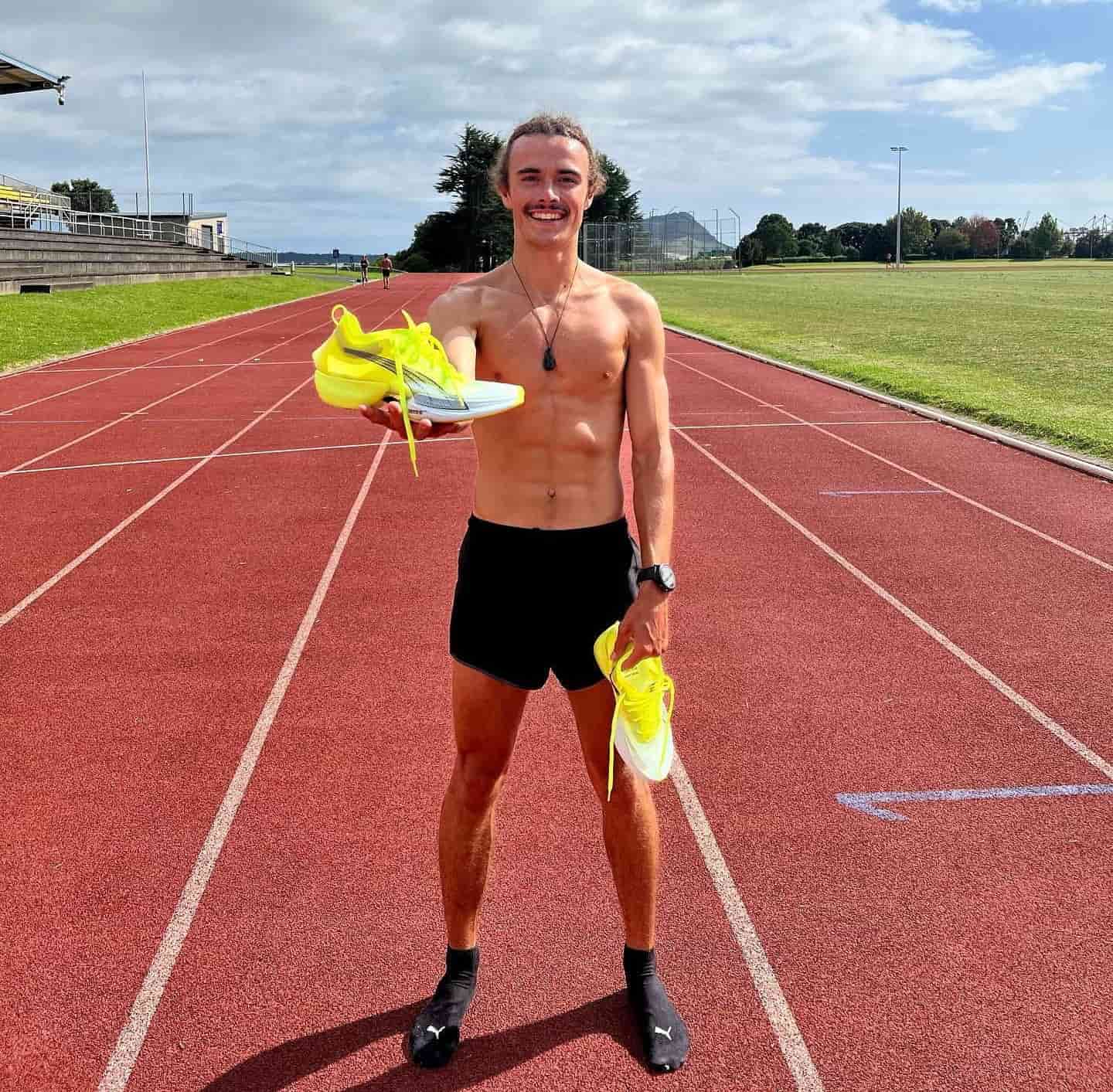 Un homme torse nue sur une piste d’athlétisme avec ses chaussures de running PUMA jaunes dans ses mains