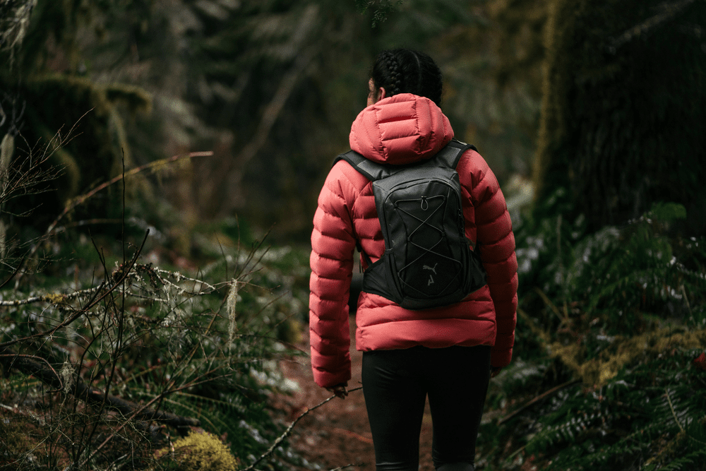 Vue de dos d'une femme en tenue de trail PUMA marchant en forêt