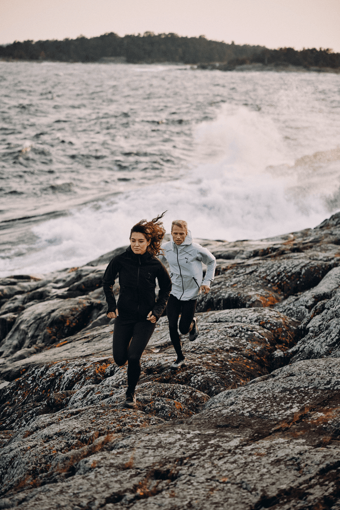 Un homme et une femme courent sur des rochers avec la mer en fond