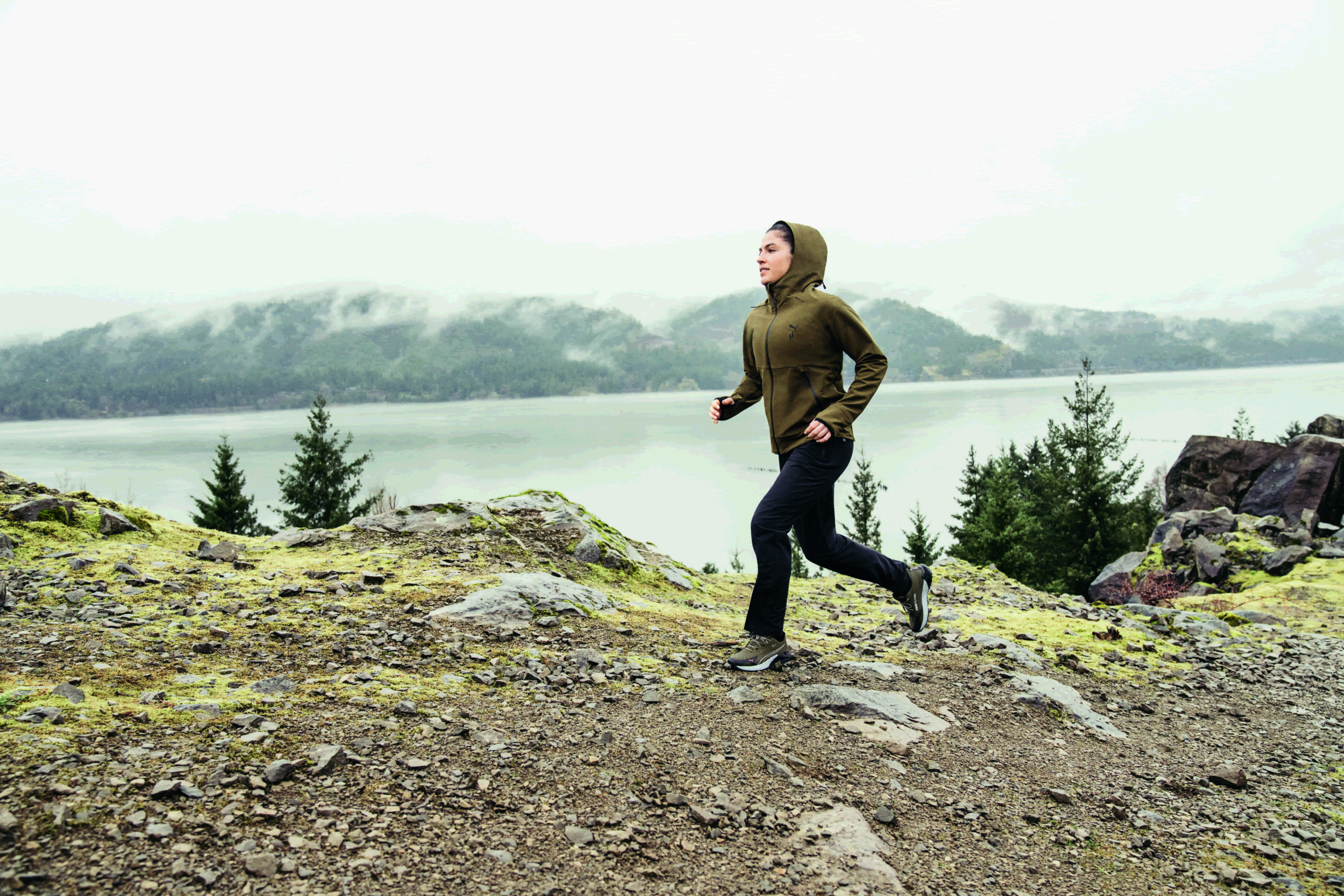 Vrouw is in koude omstandigheden aan het trailrunnen op een pad langs een meer met bergen op de achtergrond