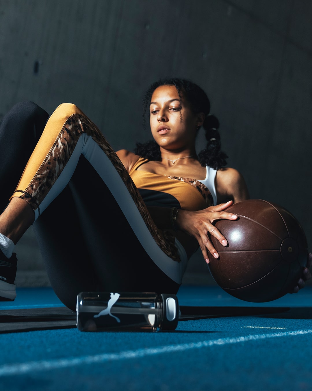 Athletin in schwarz-ocker Sport-BH und Leggings von PUMA macht Side Crunches mit Gewichtsball im Fitnessstudio