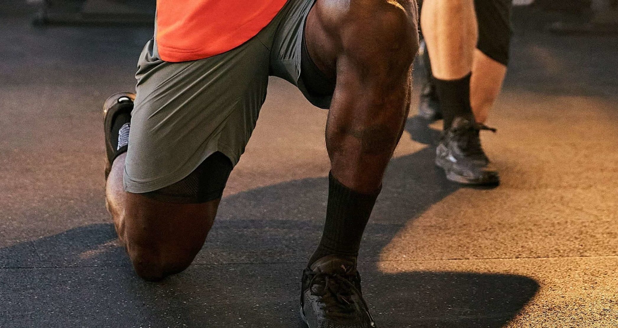 Close-up der Beine eines Mannes in grauen PUMA Shorts und schwarzen PUMA Schuhen bei Ausfallschritt-Übung im Fitnessstudio