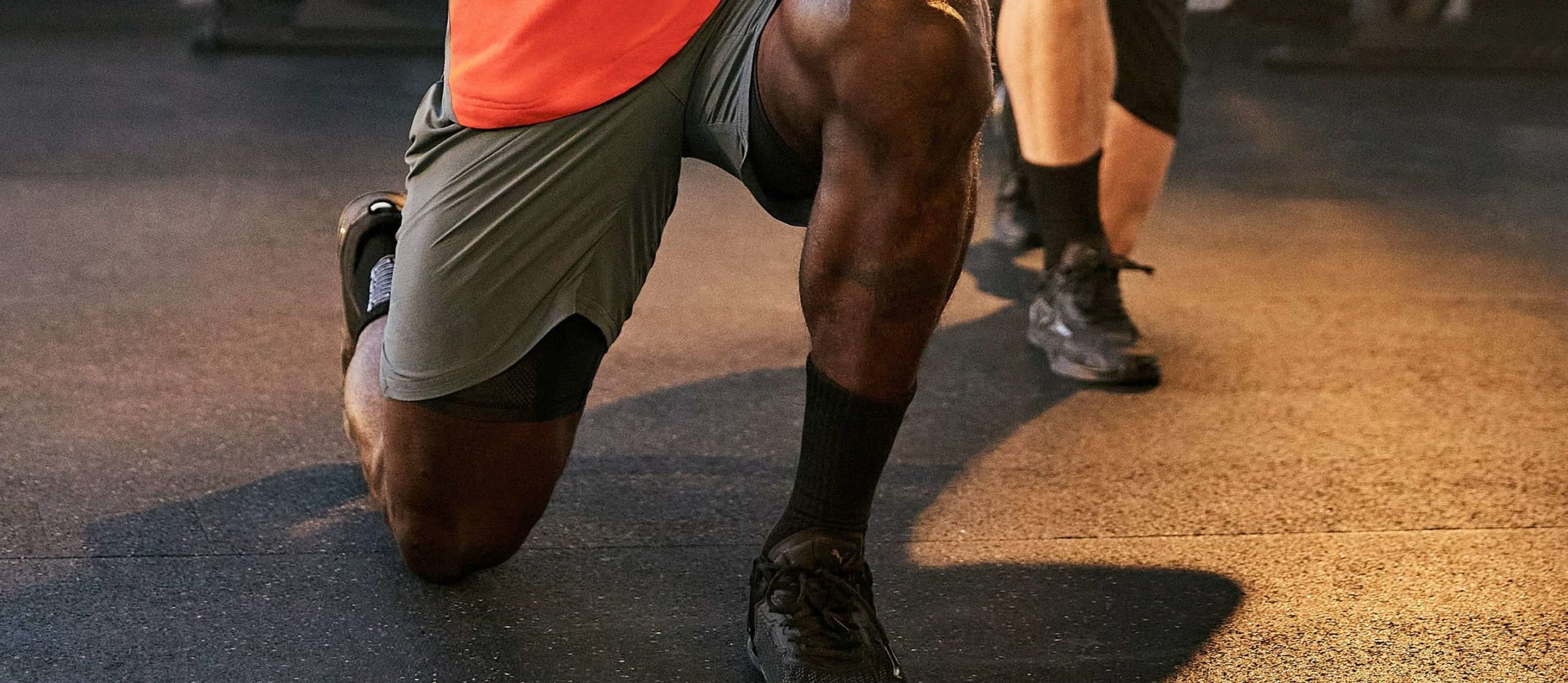 Close-up der Beine eines Mannes in grauen PUMA Shorts und schwarzen PUMA Schuhen bei Ausfallschritt-Übung im Fitnessstudio