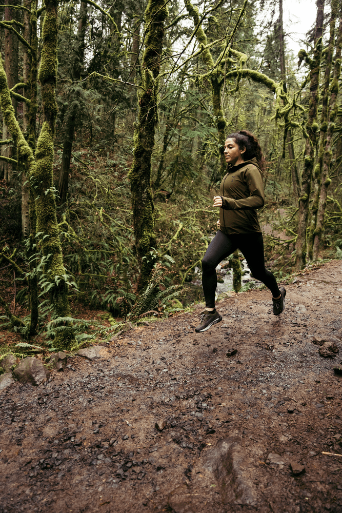 Läuferin beim Trailrunning durch den Wald gekleidet in schwarzer PUMA Laufhose, einer Laufjacke in olivgrün-schwarz und den neuen PUMA SEASONS Fast Trac GTX Trailrunningschuhen in olivgrünschwarz