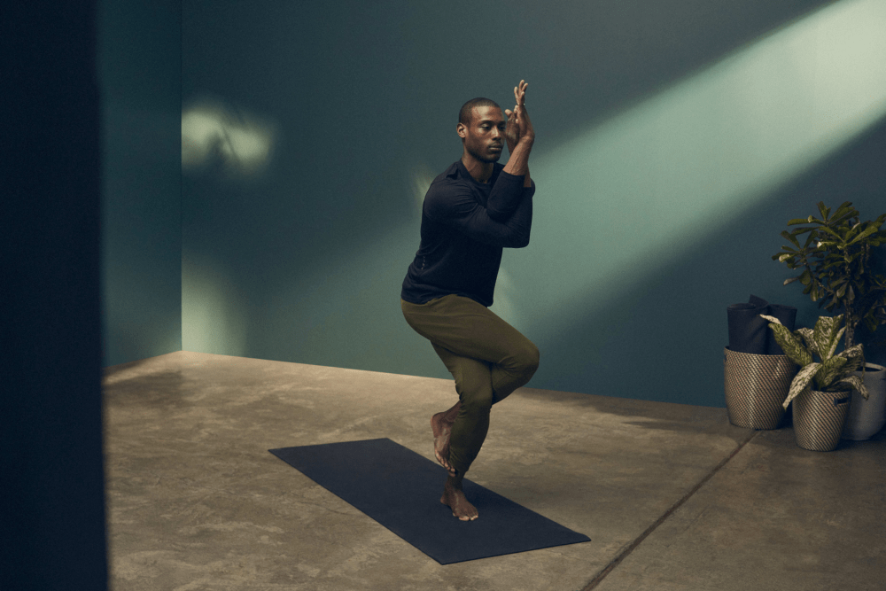 Mann in Yoga Studio gekleidet in schwarzem PUMA Langarm Shirt und dunkelgrüner Yogahose macht Eagle Pose