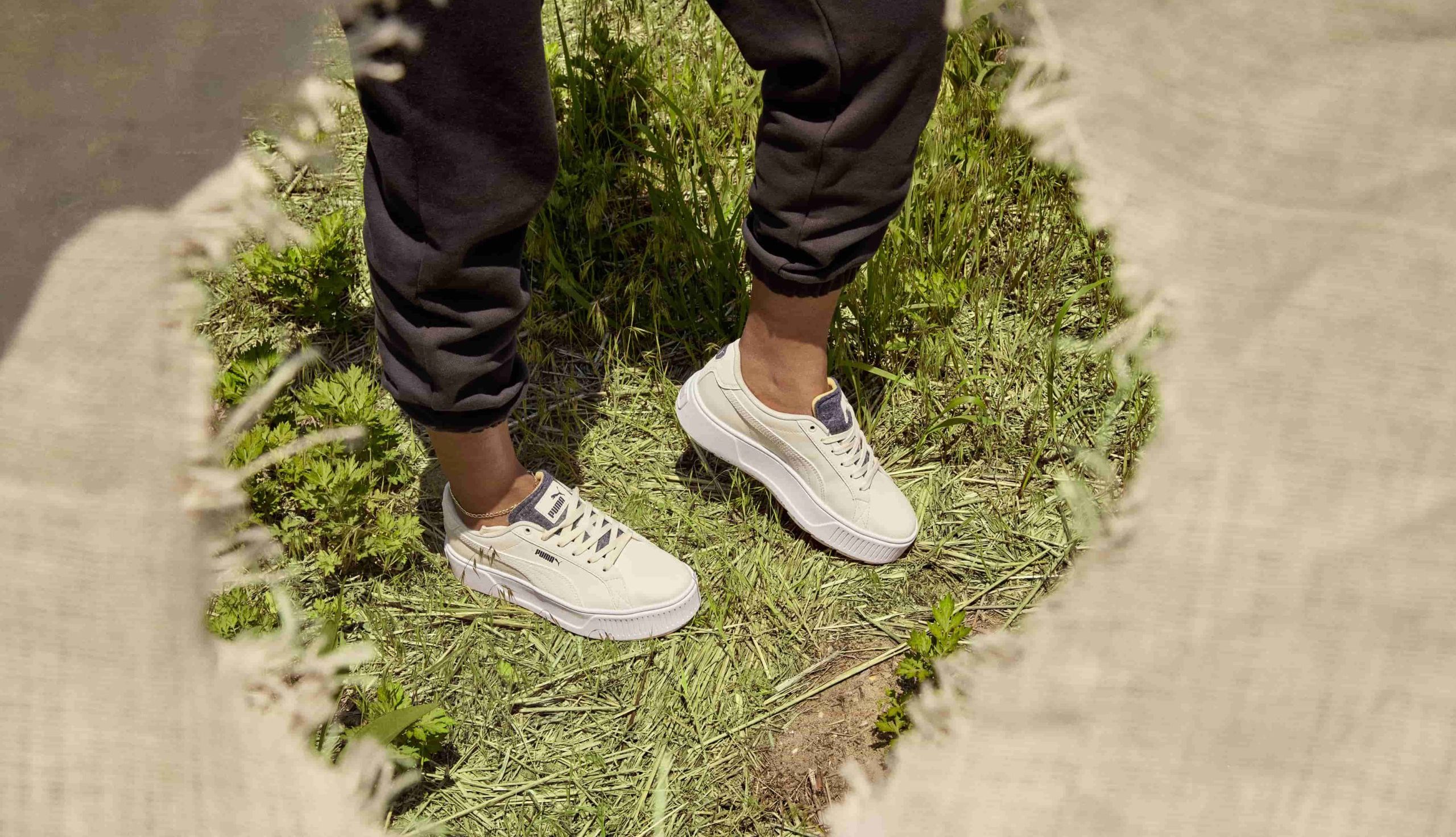 Een close-up van iemand die in het gras staat en duurzame PUMA sneakers draagt