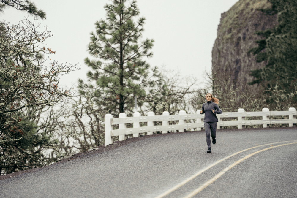 Vrouw is in de regen aan het hardlopen op een verharde weg in de bergen
