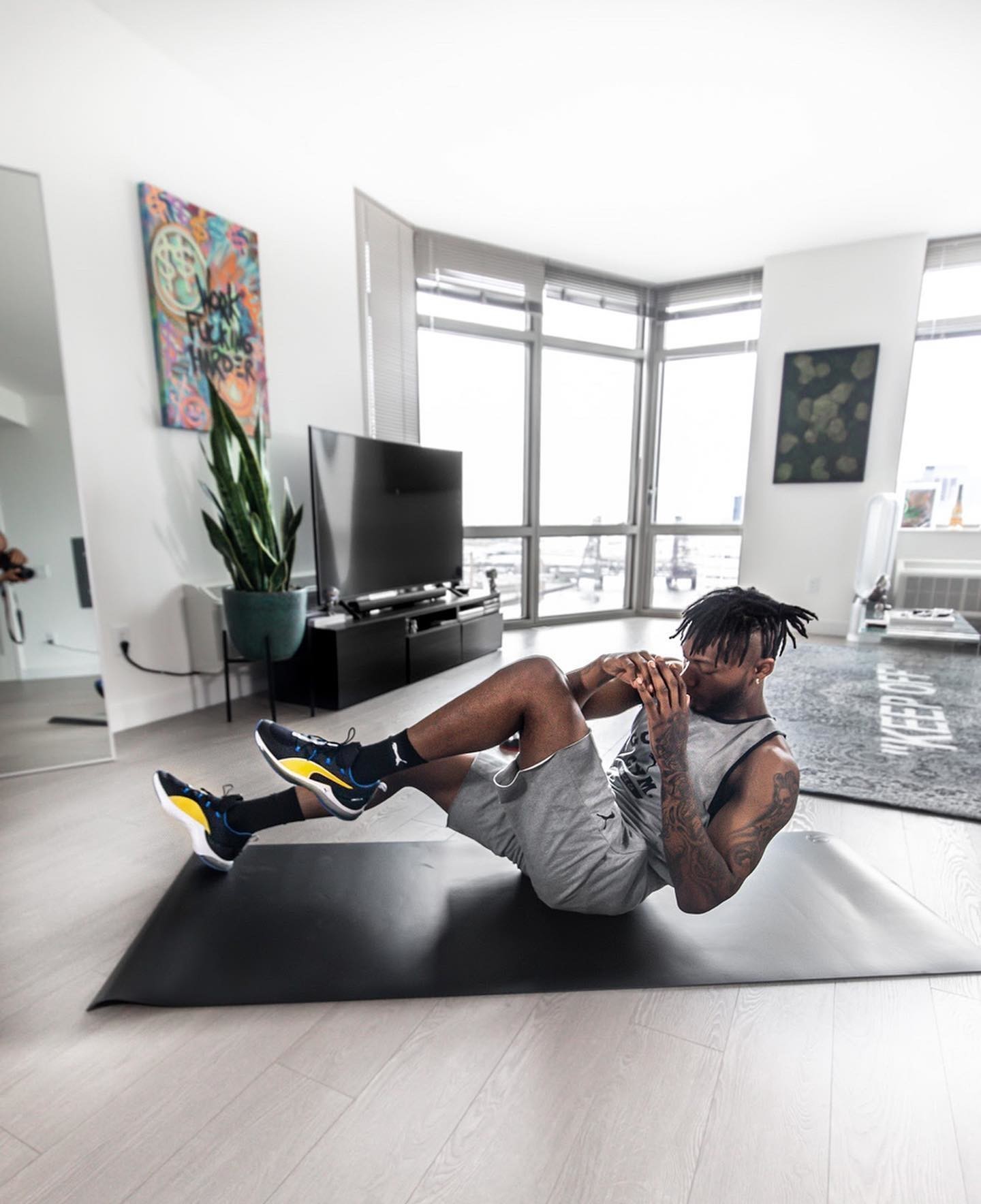 Sportler in grauen PUMA Shorts und grauem Tank Top wie schwarz-gelben Trainingsschuhen beim Side Crunches Core-Workout zuhause