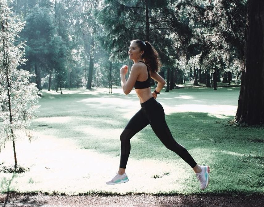 Vrouw is in de zon in een park aan het hardlopen in een lange sportlegging en sport-bh