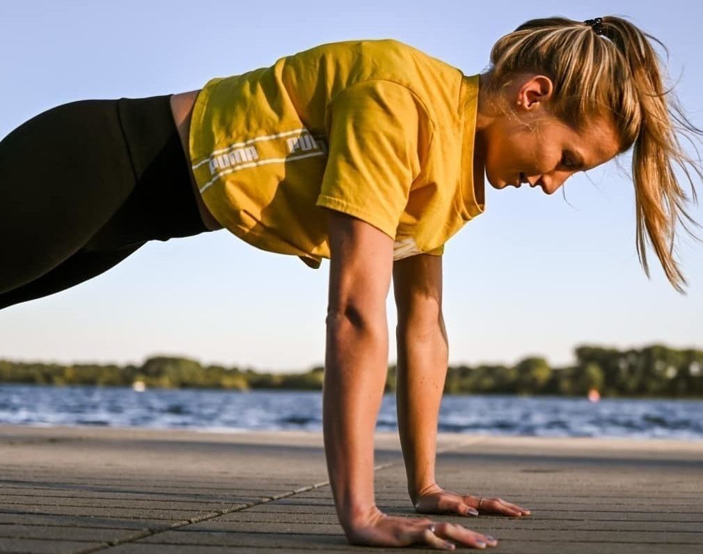 Sportlerin in schwarzen Leggins und gelben PUMA T-Shirt macht High Plank