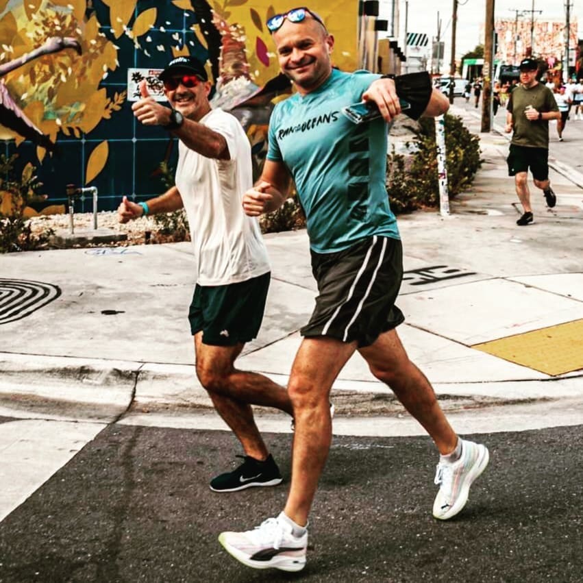 Deux hommes en train de courir sourient et font signes au photographe