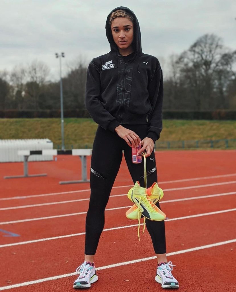 Een vrouw op een atletiekbaan houdt een paar PUMA hardloopschoenen beet