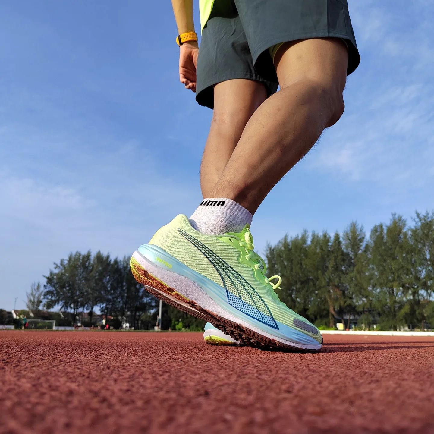 Person in kurzen Laufshorts und hellgrün-blauen PUMA Laufschuhe auf Sportplatz