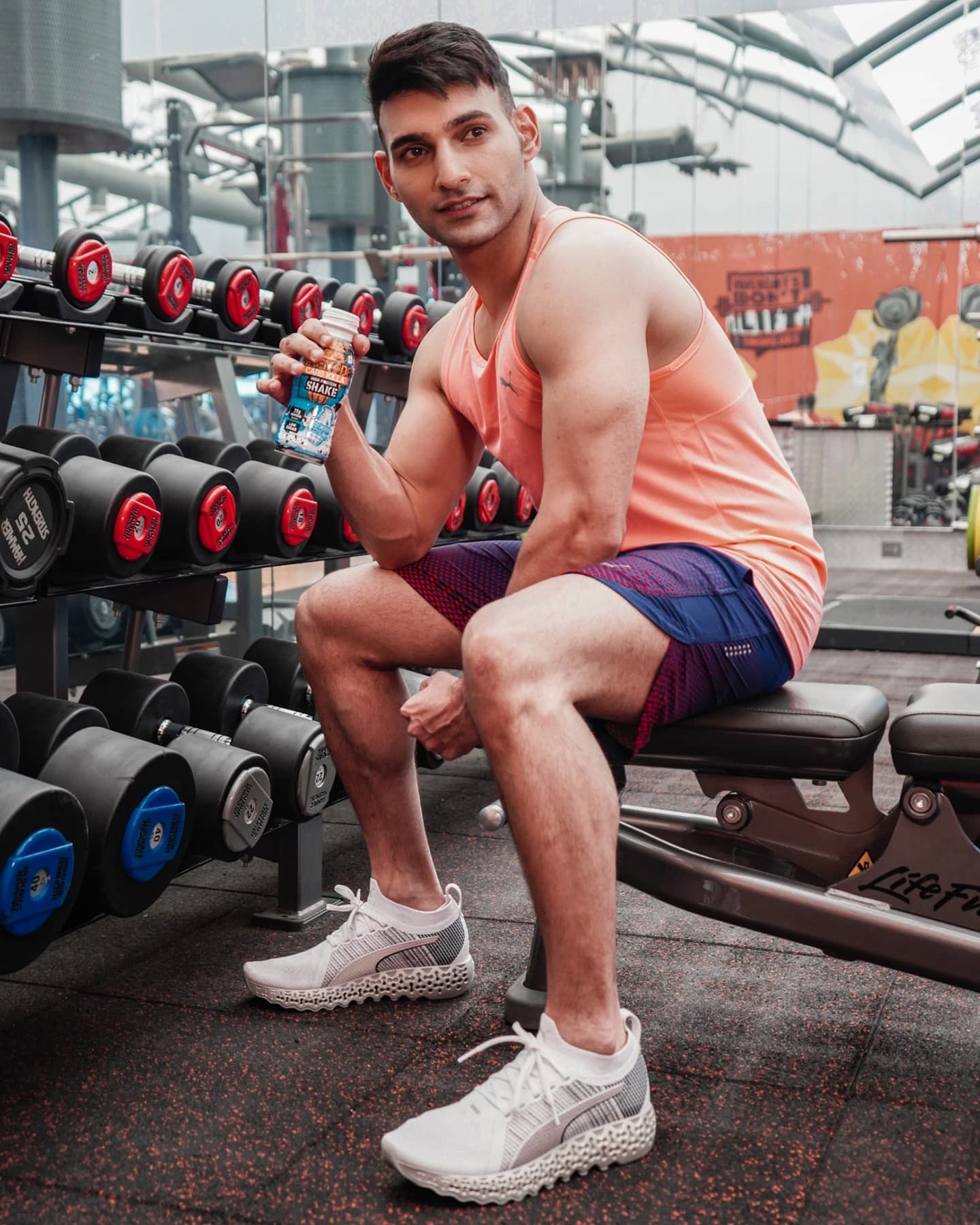 Un homme en tenue de fitness PUMA est assis sur un banc de muscu dans une salle de fitness