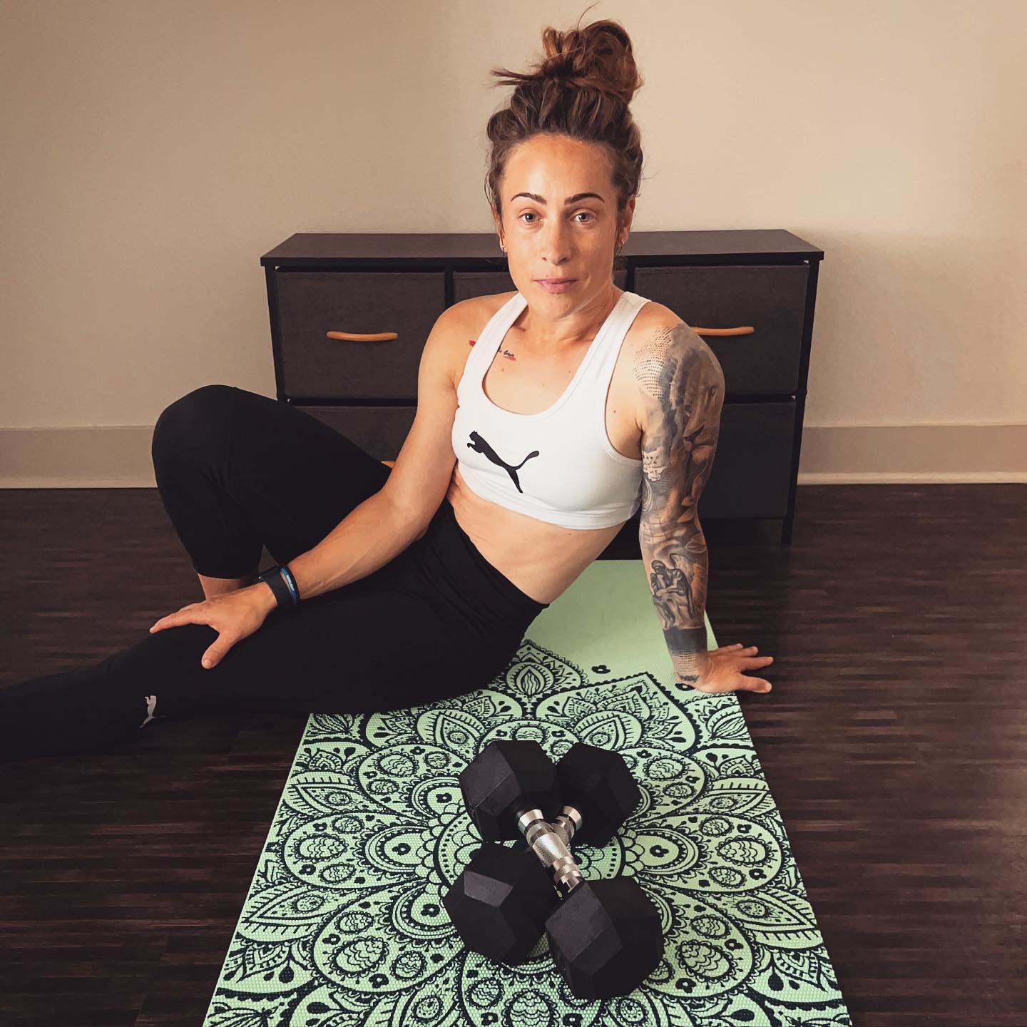 Une femme en tenue de fitness PUMA est assise sur un tapis de yoga avec deux haltères devant elle
