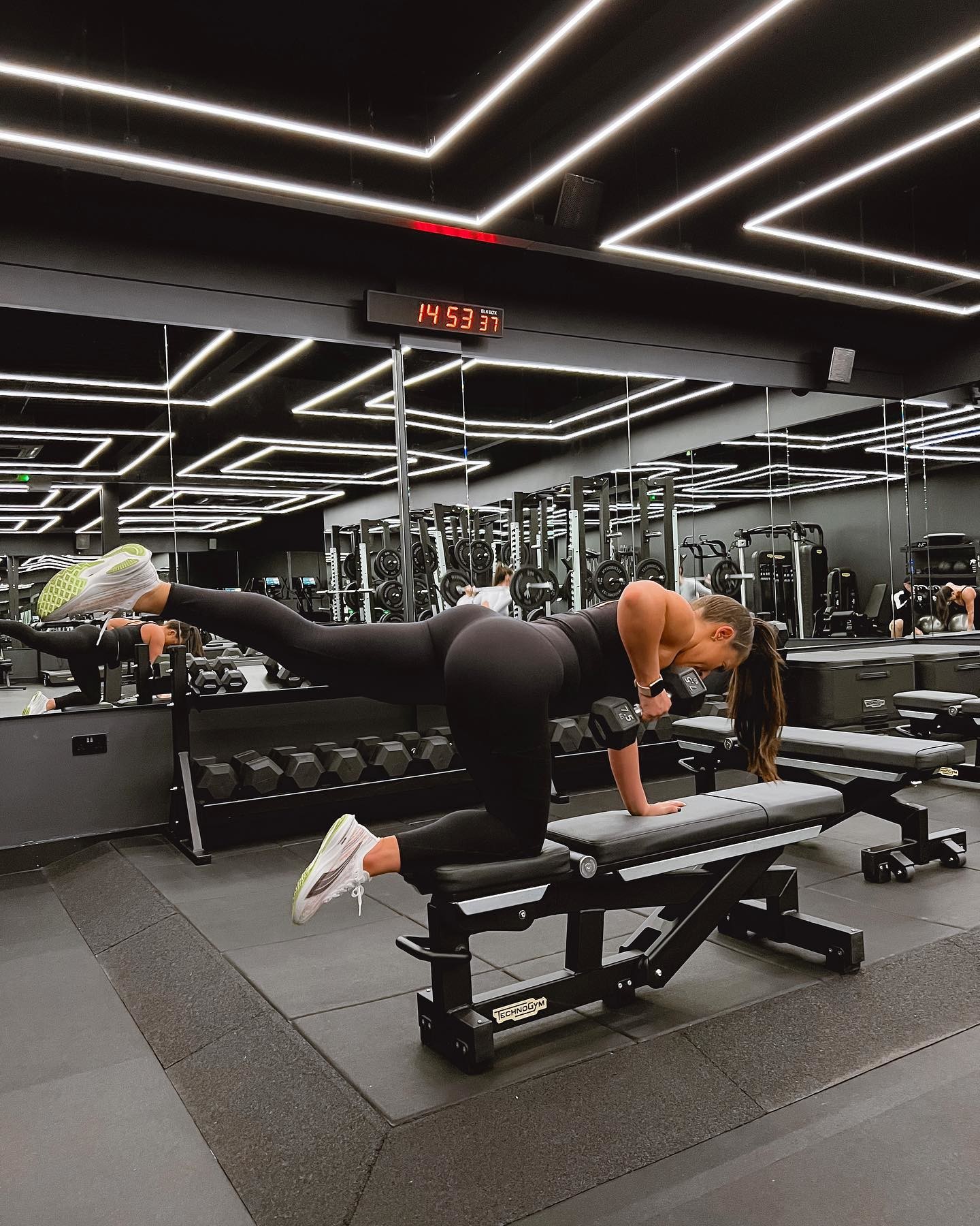 Une femme en tenue de fitness PUMA noire fait des exercices avec haltère dans une salle de fitness