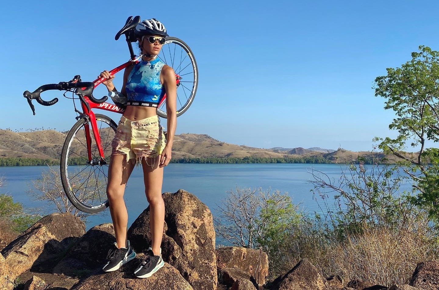 Une femme se tient debout sur des rochers et porte son vélo sur l’épaule